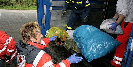 Vl. DRK Helferinnen und Helfer des DRK-Siegen-Nord sowie des THW Siegen beim Entladen der Kleiderspenden auf einen bereitgestellten LKW.