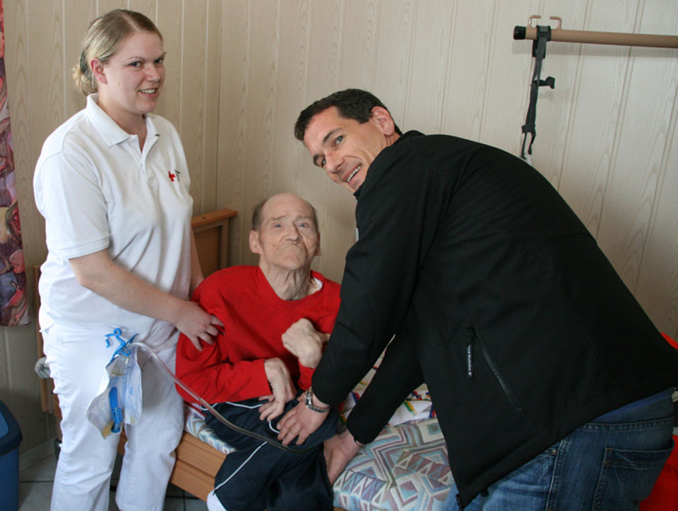 Vl. DRK-Schwester Christine Renard der Sozialstation Siegen erhält Hilfe von Jens Kamieth, um den Patienten Dieter Jäckel nach seiner Grund- und Behandlungspflege in seinen Spezialrollstuhl zu setzen.