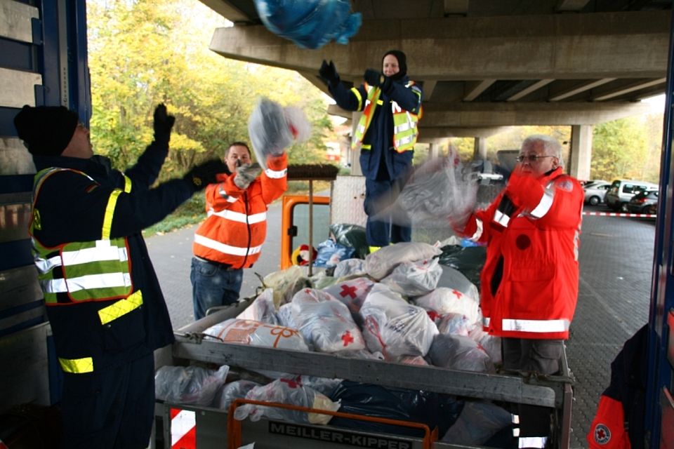 Bildunterschrift: Helfer des DRK-Siegen-Nord, THW und der Stadt Siegen laden an der Sammelstelle Geisweid, die eingesammelten Kleiderspenden aus.